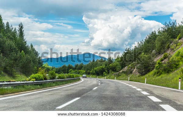 Autobahn or highway in\
the mountains with clear marking surrounded by vibrant green trees\
under blue sky. Stunning view and mountain in the background. The\
Alps, Austria