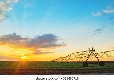 Automated farming irrigation sprinklers system on cultivated agricultural landscape field in sunset - Shutterstock ID 325486718
