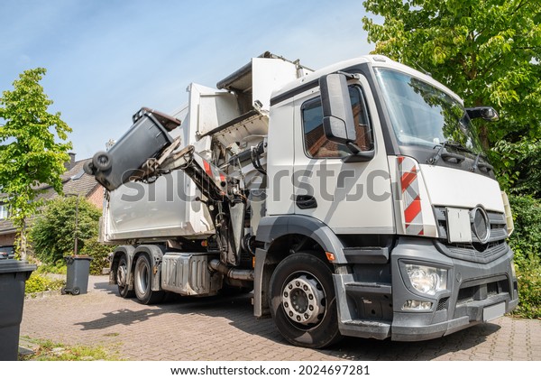automated garbage\
collection - hydraulic side loader of a white garbage truck grabs\
the garbage can to empty\
it
