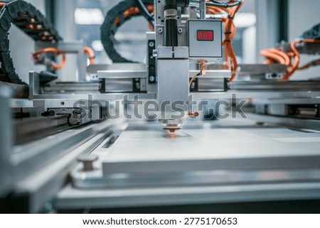 Automated laser cutting machine working on industrial sheet material. Precision laser cutting head processing sheet material on a modern automated production line in a high tech factory environment.