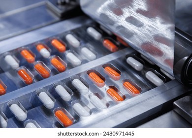 automated medicine packaging machine for orange and white capsules. Pharmaceutical production line with blister packs. Manufacturing and healthcare concept. Close-up shot. - Powered by Shutterstock