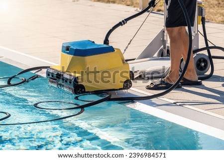 Pool cleaning robot being placed by a person next to a swimming pool