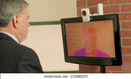 Automated Thermal Imaging Temperature Detection Being Used Due To COVID19 Before Allowing A Man To Enter Into This Business Office.