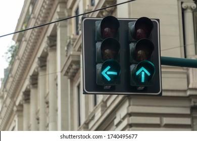 An automated traffic light in the city turned green. Arrow signs are showing straight and left directions to go ahead and move on.