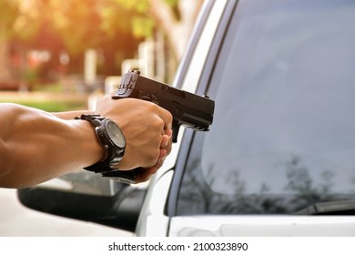 Automatic 9mm pistol holding in hand in front of the front car, blurred background, concept for assassination, robbery, gangster, vip protection, mafias and car thief.