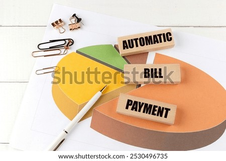 Automatic bill payment text on wooden blocks with a pie chart, pen, and office supplies on desk . 