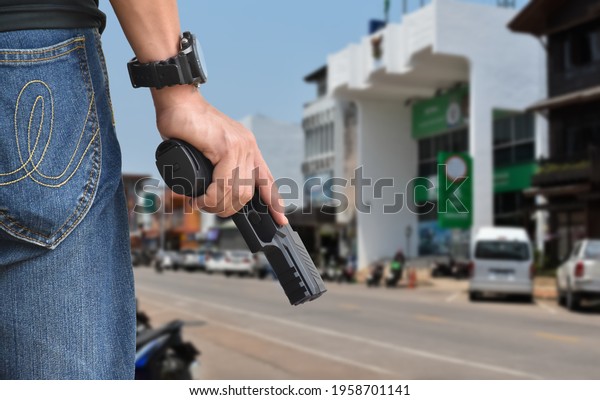 Automatic black\
9mm pistol gun holding in hand and ready to shot, concept for banks\
robbery, security, gangster and mafia on the road in the rural\
city, blurred street\
background.