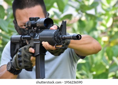 Automatic Black Airsoft Or Bb Gun Holding In Hands, Aiming To The Target Shooting And Ready To Shoot. Selective Focus On Gun Barrel Grip, Blurred Background. Shooting Sports And Training Concept.