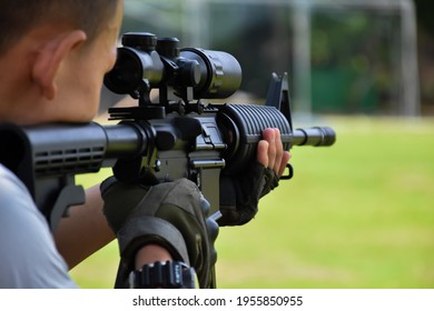 Automatic Black Airsoft Gun Or BBGUN Holding In Hands, Aiming To The Target Shooting And Ready To Shoot. Selective Focus On Gun, Blurred Background. Shooting Sports And Security Training Concept.