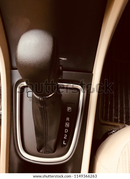 Automatic car gear shift lever. Black leather\
knob and beige\
upholstery.