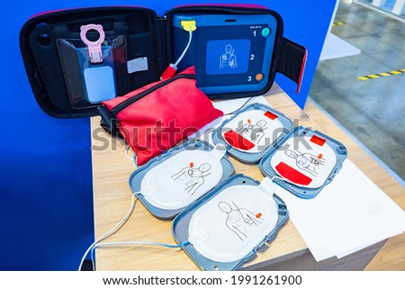 Automatic external defibrillator. Portable defibrillator on a wooden table. Defibrillator for medical care. Device for provision of emergency medical care. Automatic cardioverter with nursing manual