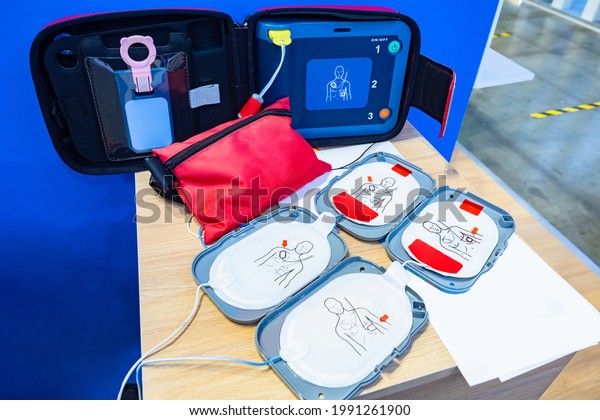 Automatic external defibrillator. Portable\
defibrillator on a wooden table. Defibrillator for medical care.\
Device for provision of emergency medical care. Automatic\
cardioverter with nursing\
manual