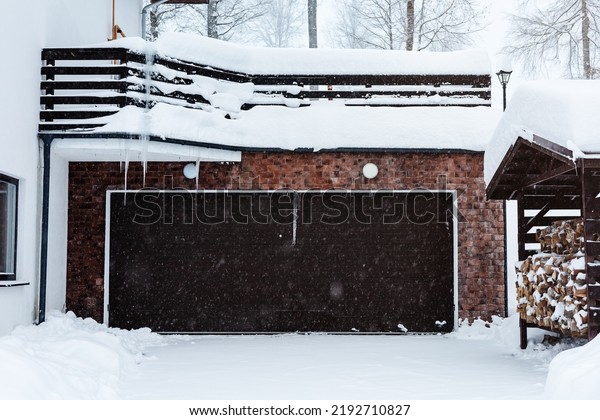 Automatic garage door of a cottage in a\
snowfall. Winter house with automatic garage doors. Mansion in the\
winter forest. Winter courtyard of a private\
cottage