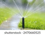 Automatic garden sprinkler in a public park. Gardening equipment. Watering the grass on lawn a hot sunny summer day