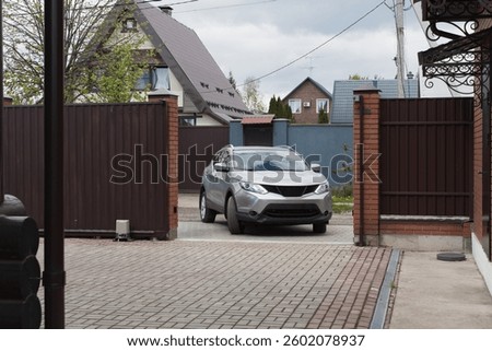 automatic gates allowing a silver SUV to enter a private residential area. The secure entrance, surrounded by brick and metal fencing, highlights smart home technology, security, and convenience.