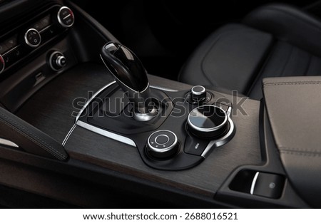 Automatic gear selector and driving mode knobs in luxury car. Automobile interior in dark tones, close-up view of bottom part of center console with automatic gear selector and driving controls.
