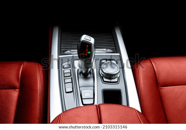 Automatic gear stick of a modern car. Multimedia\
and navigation control buttons. Car interior details. Transmission\
shift. Red leather\
interior