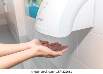 Automatic Hand Dryer In Public Toilet Or Restroom Hygiene Concept. A Man Hands Using Utomatic Hand Dryer In Bathroom.