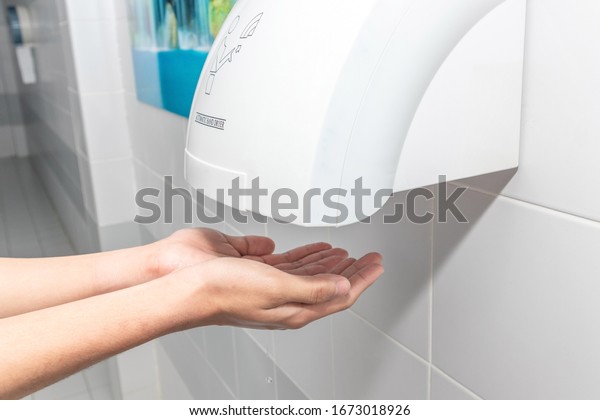 Automatic\
hand dryer in public toilet or restroom hygiene concept. A man\
hands using utomatic hand dryer in\
bathroom.