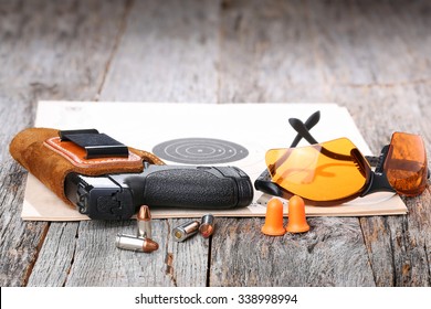 Automatic Handgun With Leather Holster, Bullets And Safety Glasses On A Wooden Background.