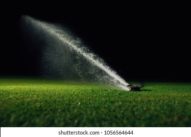 automatic lawn sprinkler spraying water over golf course green grass at night