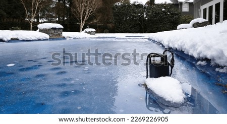 Automatic pool pump in ice and slush after snow storm. Inground backyard pool with black pool pump submerged in deep frozen water. Winterizing pool for cold or freezing temperature. Selective focus. 