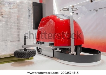 Automatic red robotic pallet wrapper during work at package trade show, warehouse. Industrial, equipment, technology concept