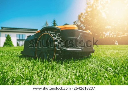 Automatic robotic lawn mower on a green lawn with modern house in background. Grass lawn mower robot in sunny summer day.