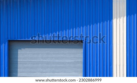 Automatic roller shutter door and white stripe on blue corrugated metal wall of warehouse building