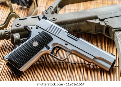 Automatic silver airsoft gun placed next to the automatic rifle. Put on bamboo floor Have bullets on the side.
