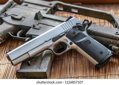 Automatic silver airsoft gun placed next to the automatic rifle. Put on bamboo floor Have bullets on the side.