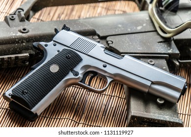 Automatic silver airsoft gun placed next to the automatic rifle. Put on bamboo floor Have bullets on the side.