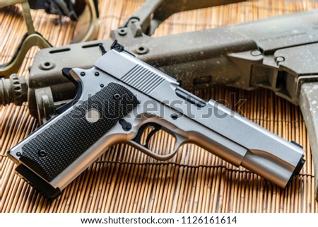 Automatic silver airsoft gun placed next to the automatic rifle. Put on bamboo floor Have bullets on the side.

