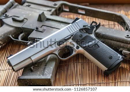 Automatic silver airsoft gun placed next to the automatic rifle. Put on bamboo floor Have bullets on the side.
