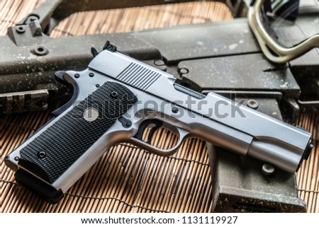 Automatic silver airsoft gun placed next to the automatic rifle. Put on bamboo floor Have bullets on the side.