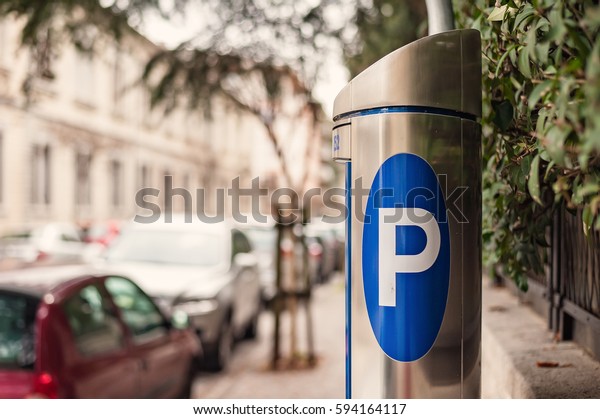Automatic ticket machine parking on\
a city street with blurred cars. Blue sign of parking\
cars.