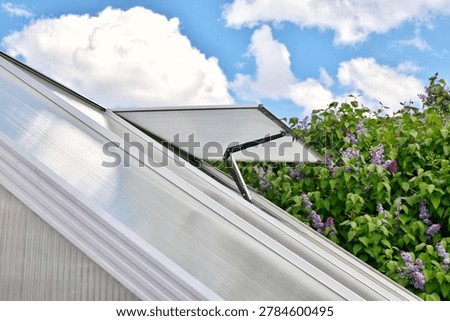 An automatic ventilation window in a modern greenhouse against the sky. Metal opening system, thermal actuator. Smart garden concept.