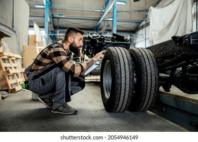 An auto-mechanic crouching next to a tire with a tablet in his hands and checking on it. Worker in the auto-mechanic workshop