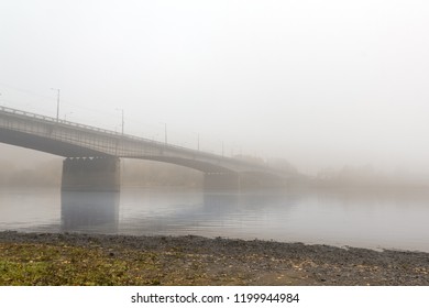 Automobile big bridge stretched across a calm river, wrapped in a dense autumn gray fog - Powered by Shutterstock