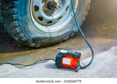 An Automobile Compressor In Soft Focus Inflates A Flat Car Tire. Selective Focus. Shot In Backlight And Sun Glare.