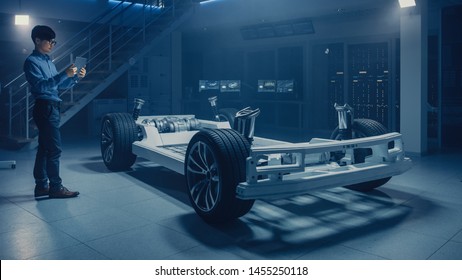 Automobile Engineer Working On Electric Car Chassis Platform, Using Tablet Computer Augmented Reality With 3D CAD Software Modelling. Innovative Facility: Vehicle Frame With Wheels, Engine, Battery