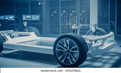 Automobile Engineers Discussing And Designing Electric Car Chassis Platform, Using Tablet Computers With 3D CAD Software. In Automotive Innovation Facility Vehicle Frame With Wheels Engine And Battery