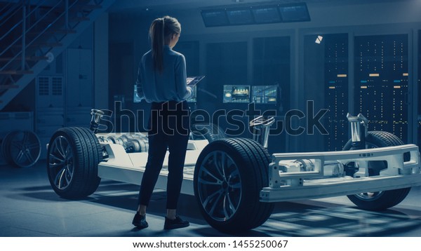Automobile Female Engineer Working on Electric Car\
Chassis Prototype, Using Tablet Computer Augmented Reality with 3D\
CAD Software Modelling. Innovative Facility: Vehicle Frame with\
Wheels, Engine