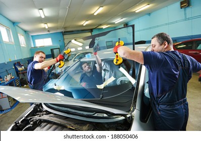 Automobile glaziers workers replacing windscreen or windshield of a car in auto service station garage