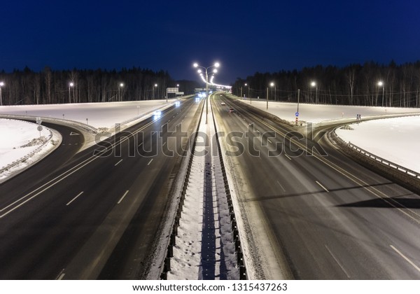 Automobile highway on a winter night\
against the background of a forest and dark blue\
sky