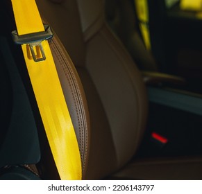 Automobile leather seat of a modern luxury car with a yellow safety belt. Yellow seat belt in a sports car close-up, blurry background. Brown leather car seat. Fasten your seat belts.