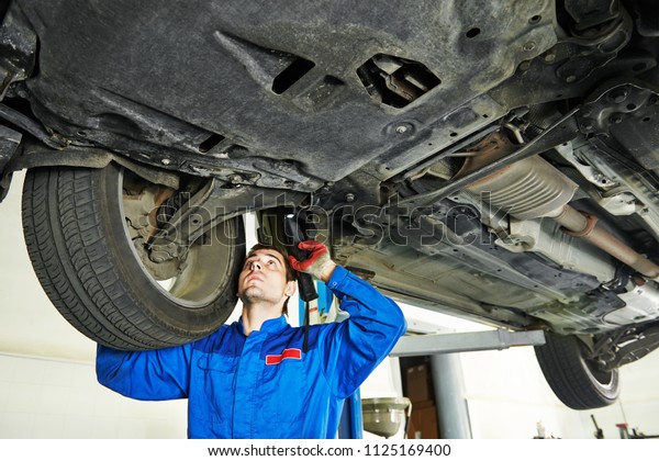 Automobile mechanic inspecting car suspension in\
service station