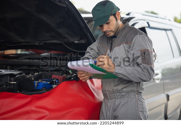 Automobile mechanic man writing to the clipboard\
checking car damage broken part condition. diagnostic and repairing\
vehicle at garage automotive, Concepts of car care check and full\
services
