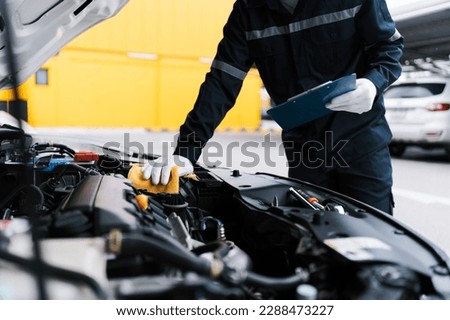 Automobile mechanic repairman checking a car engine by inspecting and writing to the clipboard the checklist for repair machine and car service for maintenance and maintenance check concept.