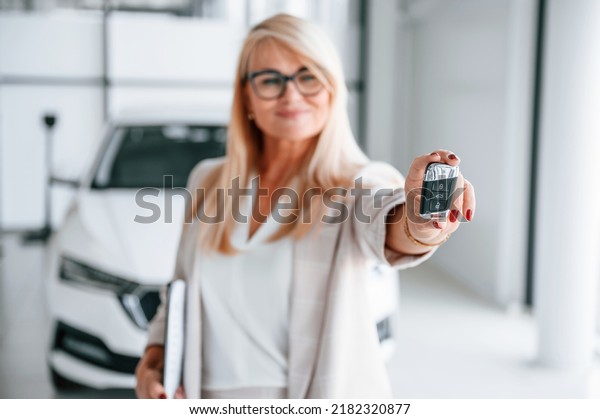 Automobile owner is holding keys. Woman in\
white formal clothes is in the car\
dealership.